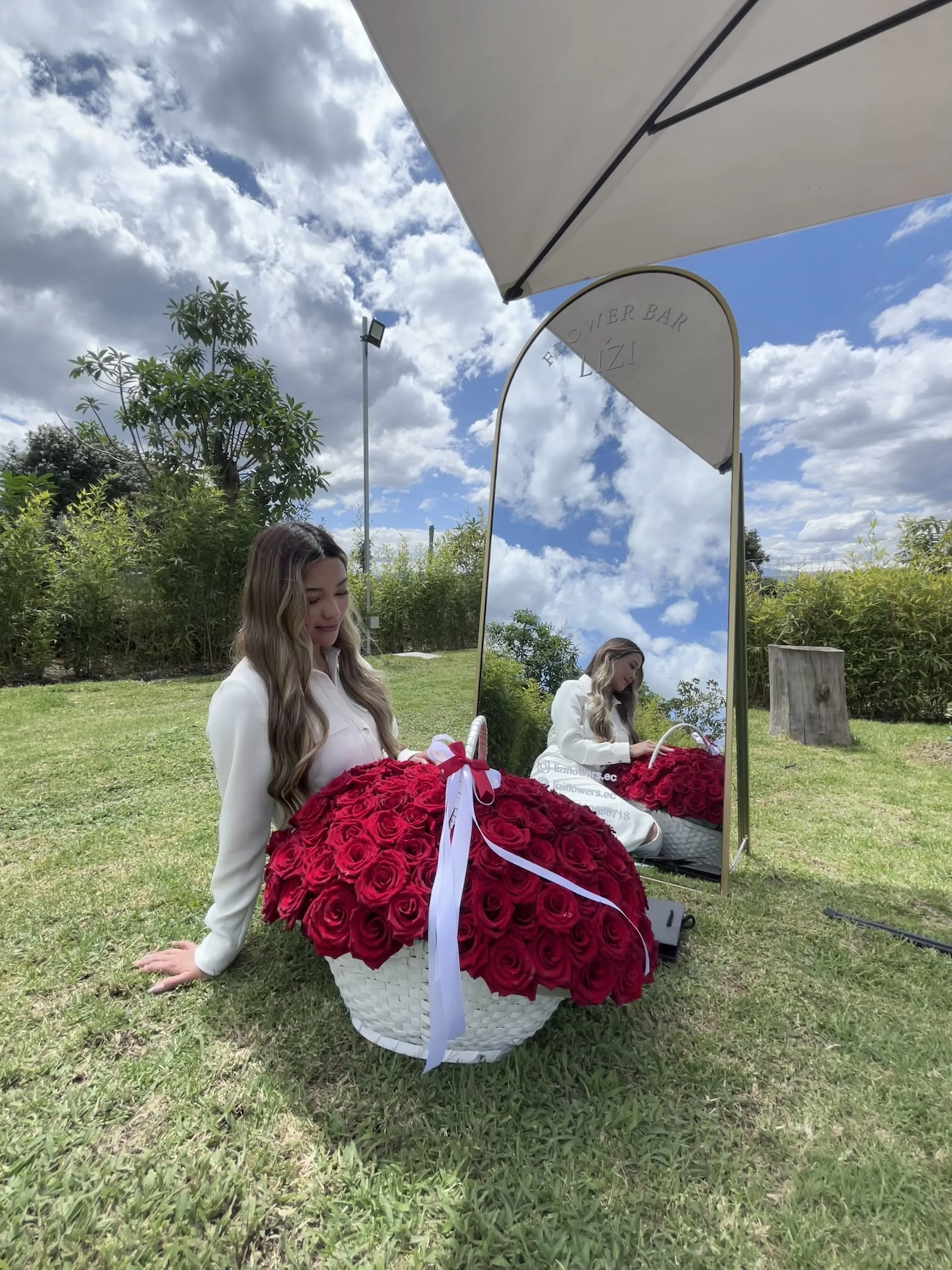 Chica sentada con una canasta de rosas rojas frente al espejo Flower Bar de Lizi